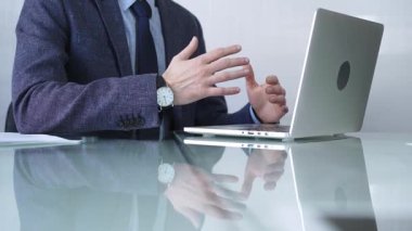 Mavi ceket giyen işadamı, modern bir ofisteki cam bir masadaki dizüstü bilgisayarla çevrimiçi iletişime odaklanarak üretkenlik ve konsantrasyon gösteriyor. İş veya denetim kavramı.