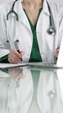 Kadın doktor, pano kullanıyor ve tıbbi bir ofisteki cam masaya notlar alıyor, dikey açıdan yakından bakıyor. Tıp konsepti.