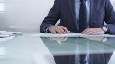 Mavi ceketli bir işadamı modern ofis ortamında cam bir masada belgeleri tutarken önemli evrakları inceliyor. İş adamları veya denetim kavramı.