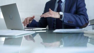 Mavi takım elbiseli bir işadamı, elleri cam ekrandaki dizüstü bilgisayarın yanında otururken parlak bir ofiste, internet iletişiminde, yakın çekim görüntüsünde oturuyor. İş konsepti.