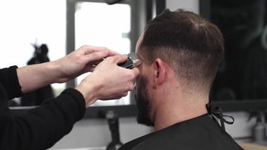 Moda bir berber dükkanında elektrikli jiletle saç kesen profesyonel berber, şık ve modern bir saç kesimi yaparken aynı zamanda rahat bir tımar deneyimi sağlıyor.