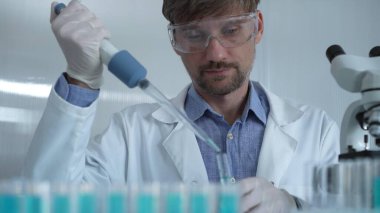 Laboratuvar önlüğü ve güvenlik gözlüğü takan bilim adamı deney tüpüne sıvı atmak için mikropipet kullanıyor. Portre görüntüsü. Tıp ve Bilim.