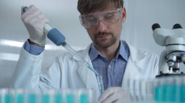 Laboratuvar önlüğü ve güvenlik gözlüğü takan bilim adamı deney tüpüne sıvı atmak için mikropipet kullanıyor. Portre görüntüsü. Tıp ve Bilim.
