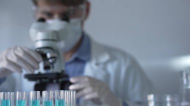 Laboratuvar tüpleri odaklandı, yakın görüş. Beyaz koruyucu eldivenli bilim adamı araştırmacı arka planda mikroskop kullanıyor. Tıp ve Bilim.