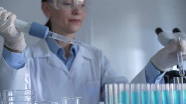 Beyaz eldivenler ve güvenlik gözlüğü takan bir bilim adamı kadın test tüplerine sıvı atmak için mikropipet kullanıyor. Tıp ve bilim konsepti.