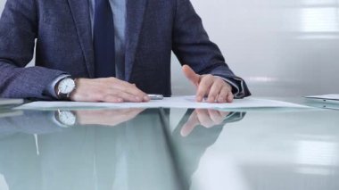 İş adamı sözleşme şartlarını inceliyor, modern ofis ortamında cam bir masada yansıması olan bir kalem kullanıyor. İş adamları veya denetim kavramı.