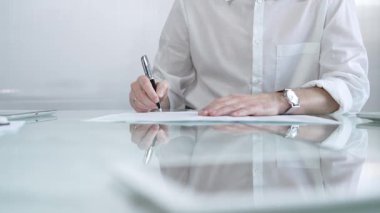 Beyaz gömlekli bir işadamı modern bir ofisteki gösterişli cam bir masada, profesyonelliğini ve çalışma ortamını gösteren bir sözleşme imzalıyor. İş adamları konsepti.