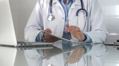 Doktor kadın, tıbbi önlüğün altına mavi bir bluz giyiyor, modern sağlık ortamında dijital tablet kullanıyor, hasta verileriyle etkileşimde, yakın plan. Tıp konsepti.