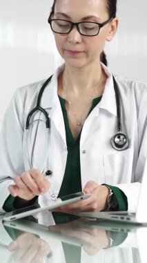 Modern sağlık ortamında dijital tablet kullanan beyaz önlüklü kadın doktor hasta verileriyle ve dikey portreyle etkileşimde. Tıp konsepti.