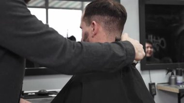 Moda bir berber dükkanında elektrikli jiletle saç kesen profesyonel berber, şık ve modern bir saç kesimi yaparken aynı zamanda rahat bir tımar deneyimi sağlıyor.