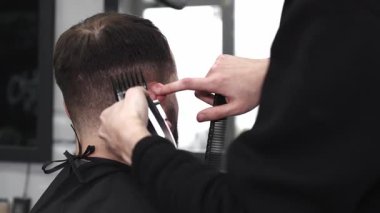 Moda bir berber dükkanında elektrikli jiletle saç kesen profesyonel berber, şık ve modern bir saç kesimi yaparken aynı zamanda rahat bir tımar deneyimi sağlıyor..
