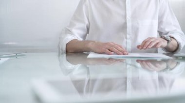 Beyaz gömlekli bir iş adamı, güncel ofis ortamında cam bir masada evrakları tutarken evrak işleriyle uğraşıyor. İş adamları konsepti.