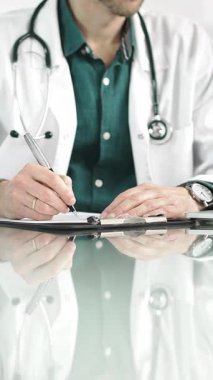 Erkek doktor bir dosya kullanıyor ve bir tıp bürosundaki cam masaya notlar alıyor, dikey açıdan yakından bakıyor. Tıp konsepti.