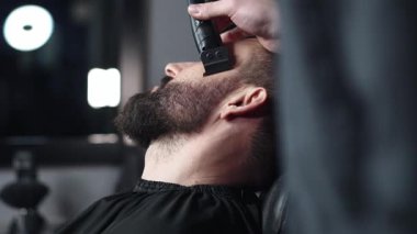 Profesyonel berber erkek müşterinin sakalını elektrikli budayıcı kullanarak dikkatlice şekillendiriyor, modern berber dükkanında titiz bir bakım ve stil sağlıyor.
