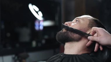 Berber müşterinin sakalını titizlikle tarar, profesyonel bir berber dükkanında stil ve bakım sağlar, yüz kıllarını özen ve uzmanlıkla güçlendirir.