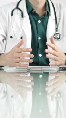 Steteskop ve laboratuvar önlüğü giyen erkek doktor, masadaki bir hastaya dizüstü bilgisayarla teşhis koymayı açıklarken elleriyle işaret ediyor. İlaç..