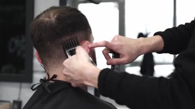 Moda bir berber dükkanında elektrikli jiletle saç kesen profesyonel berber, şık ve modern bir saç kesimi yaparken aynı zamanda rahat bir tımar deneyimi sağlıyor.