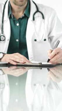 Erkek doktor bir dosya kullanıyor ve bir tıp bürosundaki cam masaya notlar alıyor, dikey açıdan yakından bakıyor. Tıp konsepti.