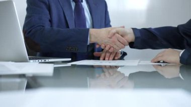 İş adamları toplantıda anlaşmaya vardıktan sonra cam masada el sıkışıyorlar. Tokalaşmanın yakın çekimi.