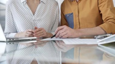 İki muhasebeci, bir dizüstü bilgisayar kullanarak ve cam bir masadaki belgeleri inceleyerek vergi denetimini tartışıyor. Vergiler, iş denetimleri.