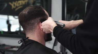 Moda bir berber dükkanında elektrikli jiletle saç kesen profesyonel berber, şık ve modern bir saç kesimi yaparken aynı zamanda rahat bir tımar deneyimi sağlıyor..