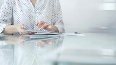 Beyaz noktalı bluzlu iş kadını modern cam bir masada çalışıyor, görevleri yönetmek ve çağdaş ofis ortamında iletişim kurmak için dijital tablet kullanıyor. İş adamları konsepti.