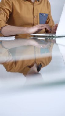 Sarı tişört giyen işadamı dizüstü bilgisayarda daktilo kullanıyor, cam masada vergiler ve denetim raporları hazırlıyor, dikey yakın çekim görüntüsü. Vergiler, iş denetimleri.