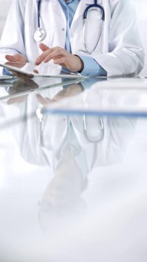 Mavi bluzlu, steteskoplu ve beyaz önlüklü tanınmayan kadın doktor modern sağlık ortamında dijital tablet kullanıyor, hasta verileriyle ve dikey görüşüyle etkileşimde. Tıp ve Bilim.
