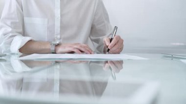 Beyaz gömlekli bir işadamı modern bir ofisteki gösterişli cam bir masada, profesyonelliğini ve çalışma ortamını gösteren bir sözleşme imzalıyor. İş adamları konsepti.