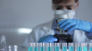 Laboratuvar tüpleri odaklandı, yakın görüş. Mavi koruyucu eldivenli bilim adamı araştırmacı arka planda mikroskop kullanıyor. Tıp ve bilim konsepti.