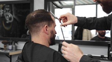 Profesyonel berber, modaya uygun bir berber dükkanında profesyonel bir makasla müşterinin saçını kesiyor, şık ve modern bir saç kesimi yapıyor, aynı zamanda rahat bir tımar deneyimi sağlıyor..
