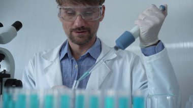 Laboratuvar önlüğü ve güvenlik gözlüğü takan bilim adamı deney tüpüne sıvı atmak için mikropipet kullanıyor. Portre görüntüsü. Tıp ve Bilim.