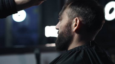 Modern bir berber dükkanında müşterilerin saçlarını ustalıkla tarayan profesyonel berber, moda ve şık bir saç stili yaratmak için titizlikle hazırlanıyor.