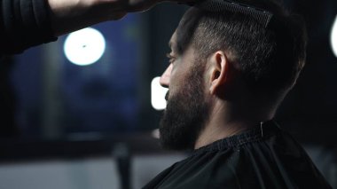 Modern bir berber dükkanında müşterilerin saçlarını ustalıkla tarayan profesyonel berber, moda ve şık bir saç stili yaratmak için titizlikle hazırlanıyor.