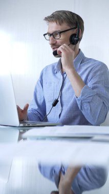 Erkek ofis çalışanı, modern iş dünyasındaki teknolojinin önemini dizüstü bilgisayar ve kulaklık kullanarak gösteriyor. İş adamları konsepti.