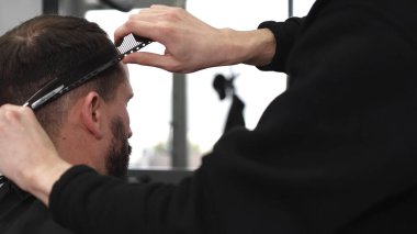 Profesyonel berber saçlarını makas ve tarakla kesiyor, modern bir berber dükkanında şık ve titiz bir saç kesimi yapıyor, müşteriler rahat ve rahatlatıcı bir deneyimden zevk alıyor.