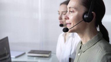 Mavi günlük bluzlu odaklı kadın çağrı merkezi operatörü müşterilerine çevrimiçi olarak yardım ediyor, müşteri desteği sağlıyor ve sorulara cevap veriyor. Çağrı merkezi operatörleri