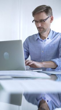 Sıradan giyimli iş adamı, modern bir ofiste verimliliği artıran temiz ve parlak bir çevreye sahip bir dizüstü bilgisayar kullanıyor. İş adamları konsepti.