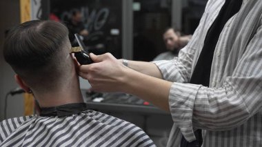Profesyonel berber müşterilerin saçlarını elektrikli makasla dikkatlice buduyor, modern bir berber dükkanında şık ve kusursuz bir saç kesimi sağlıyor.
