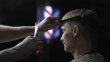 Profesyonel berber erkek müşterinin saçını makasıyla dikkatlice kesiyor modern berber dükkanının arka planında şık ve titiz bir saç kesimi sağlıyor..