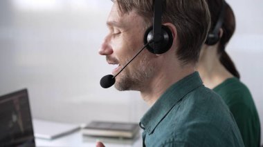 Yeşil günlük gömlekli odaklı erkek çağrı merkezi operatörü müşterilerine çevrimiçi olarak yardım ediyor, müşteri desteği sağlıyor ve sorulara cevap veriyor. Çağrı merkezi kavramı.