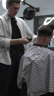 Profesyonel berber müşterilerin saçlarını elektrikli makasla dikkatlice buduyor, modern bir berber dükkanında şık ve kusursuz bir saç kesimi sağlıyor.