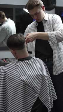 Profesyonel berber müşterilerin saçlarını elektrikli makasla dikkatlice buduyor, modern bir berber dükkanında şık ve kusursuz bir saç kesimi sağlıyor.