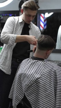 Profesyonel berber müşterilerin saçlarını elektrikli makasla dikkatlice buduyor, modern bir berber dükkanında şık ve kusursuz bir saç kesimi sağlıyor..