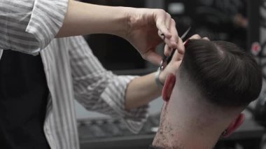 Profesyonel berber, müşterilerin saçlarını buduyor, makas ve tarakla kusursuz bir solukluk çiziyor, çağdaş berber dükkânı düzenliyor, uzman tımar ediyor.