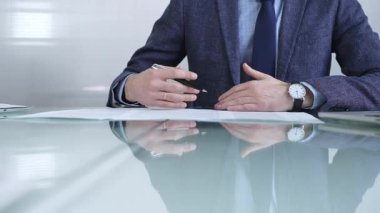 İş adamı sözleşme şartlarını inceliyor, modern ofis ortamında cam bir masada yansıması olan bir kalem kullanıyor. İş adamları veya denetim kavramı.