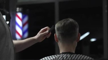 Berber, arka planda belirgin bir berber direği sergilenen hareketli bir berber dükkanında şık bir saç ve saç kesimine başlamadan önce müşterileri muayene ediyor.