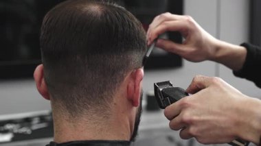 Profesyonel berber, modaya uygun bir berber dükkanında bir adamın saçını elektrikli makasla ustaca kesiyor, müşterileri daha şık ve modern bir saç stili yaratıyor.