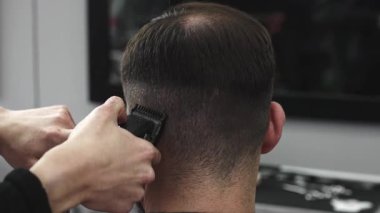 Profesyonel berber, modaya uygun bir berber dükkanında bir adamın saçını elektrikli makasla ustaca kesiyor, müşterileri daha şık ve modern bir saç stili yaratıyor.