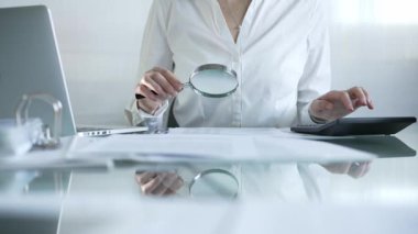 İş kadını büyüteç ve siyah hesap makinesiyle finansal verileri analiz ediyor, muhasebe ve denetleme görevlerini yerine getiriyor. Denetim ve vergi kavramı.